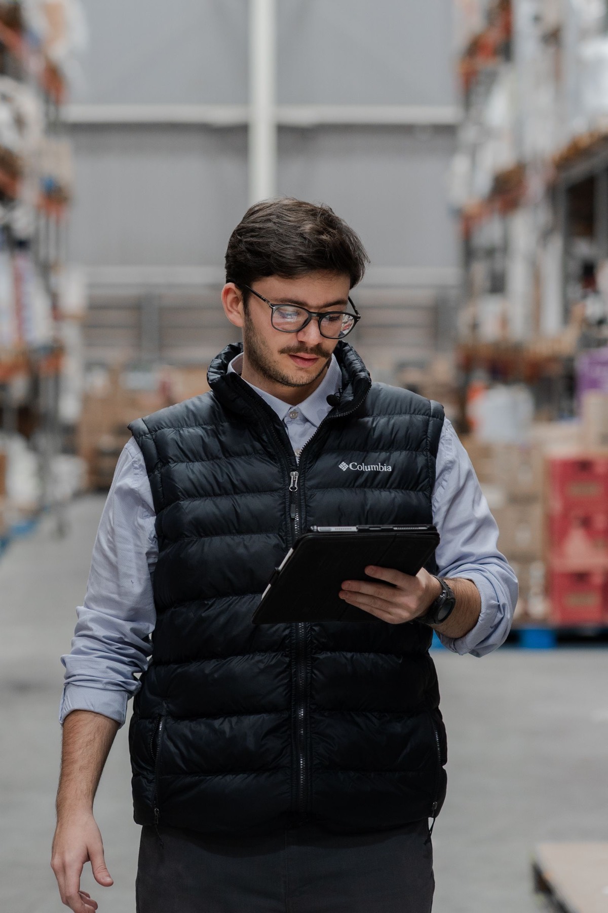 Ein junger Mitarbeiter in Weste prüft in einer Lagerhalle den Bestand auf dem Tablet.