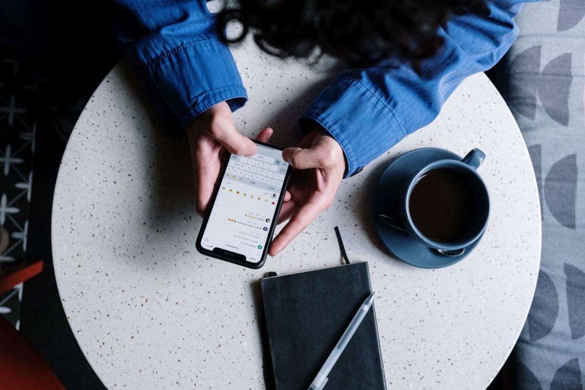 Hands hold a phone, next to it lie a notebook and a cup of coffee.